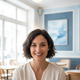 Smiling French woman in her late 20s with short dark hair, wearing a stylish top, against a blurred cafe background.