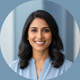 Smiling South Asian woman, mid-30s, looking at the camera with a happy expression. Soft blue and white background.