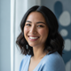Close-up portrait of a smiling young woman, diverse and authentic, with a warm, trustworthy expression against a soft blue ba